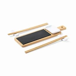 A bamboo sushi serving board featuring a black slate area, with chopsticks and a small white sauce dish.