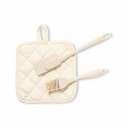A cream-coloured kitchen set featuring a pot holder and two utensils, including a spatula and a brush.