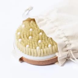 A body brush with natural bristles and a cotton pouch, featuring a round shape and a metallic base.