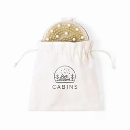 A round brush with a textured surface and white pearls, stored in a drawstring cotton bag featuring a simple logo.