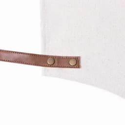 An off-white fabric bag with a brown leather strap and snap buttons.