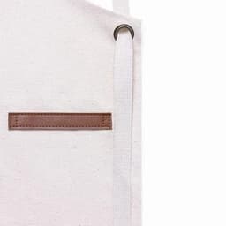 A white tote bag with a brown leather patch and a white strap. The bag features a simple design.