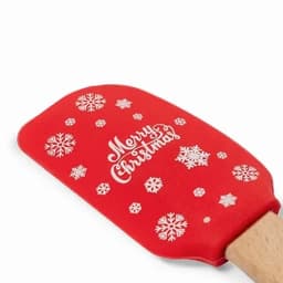 A red spatula with a wooden handle, featuring white snowflakes and "Merry Christmas" design.