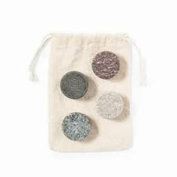 A drawstring pouch containing four round, textured stones in shades of grey, green, and brown.