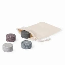A set of four round, textured stones in grey, black, and light purple, beside a drawstring pouch.