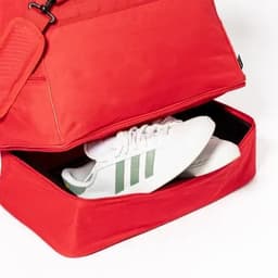 A red bag with a compartment containing white shoes with green stripes, showcasing its storage capacity.