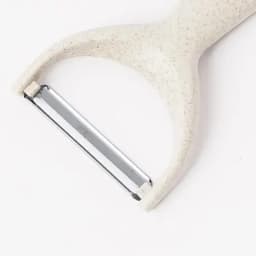 A vegetable peeler with a cream-coloured handle and a shiny metal blade. It features a simple design with a logo.