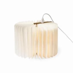 A lamp with a pleated white shade, featuring a warm glow and a grey cable for power.