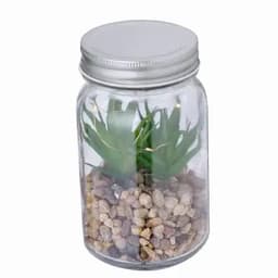 A glass jar contains artificial greenery and small pebbles, topped with a metallic lid.