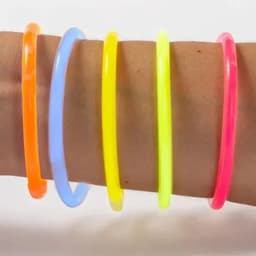 A collection of five neon glow bracelets in orange, blue, yellow, green, and pink stacked on an arm.