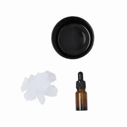 A black dish, a dropper bottle with an amber hue, and white tissue pieces are arranged together.
