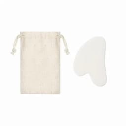 A cream-coloured pouch with a drawstring and a white gua sha tool beside it. The pouch features a simple design.