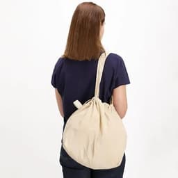 A drawstring bag in a neutral beige colour, being worn over the shoulder by a person from the back.