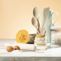 A collection of wooden kitchen utensils in a holder, alongside two eggs, a rolling pin, and a piece of pumpkin.