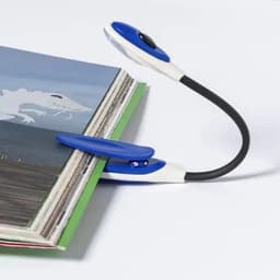 A blue and white book light rests on the edge of an open book, illuminating the pages for reading.