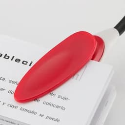 A red bookmark rests on a stack of white pages, featuring a black spine. The bookmark has a smooth, oval shape.