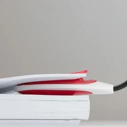 A red and white reading light rests atop a stack of white books against a grey background.
