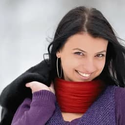 A woman wearing a red neck warmer, smiling, with long dark hair and an outfit featuring purple tones.