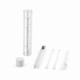 A transparent measuring cylinder with a lid, accompanied by various white measuring tools including a scoop and spatula.