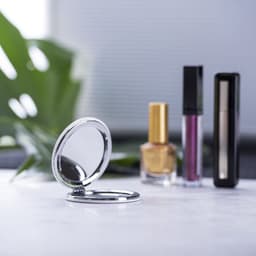 A compact mirror in a silver case, alongside three cosmetic bottles with various colours of nail polish and lip products.