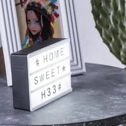 A decorative light box with white letters, set on a grey table next to a picture frame. It has a simple grey and silver design.
