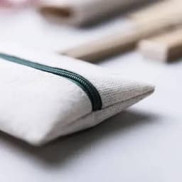 A pouch in a natural fabric with a green zipper, placed beside wooden utensils on a light background.