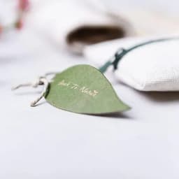 A green leaf-shaped tag with twine attached, placed on a light surface alongside a textured fabric item.