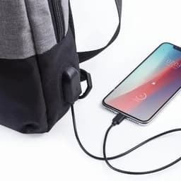 A backpack with a grey and black design, featuring a built-in USB port connected to a smartphone charging cable.