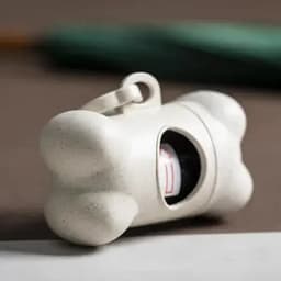 A white bone-shaped dispenser with a compartment, designed for pet waste bags. Features a small circular opening.