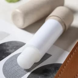 A drink bottle with a white body and a natural-toned lid, resting on a patterned surface.