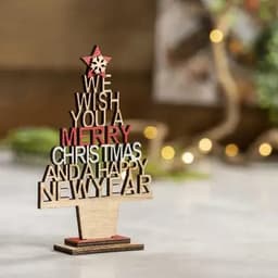 A decorative wooden sign with festive text, featuring red and natural wood hues, arranged in a Christmas tree shape.