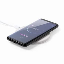 A phone is placed on a round, grey wireless charging pad with a white cable connected. The screen displays a battery percentage.