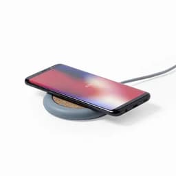 A wireless charger with a cork surface and a grey base, holding a smartphone on top.