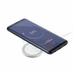 A smartphone is placed on a wireless charging pad, displaying a battery status of 84% on the screen.