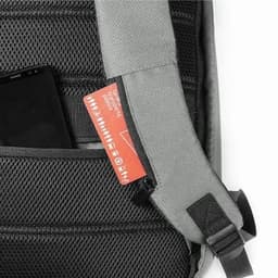 A grey backpack featuring a black mesh pocket with a phone and a red tag partially visible. It has an adjustable strap.