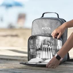 A backpack with a grey exterior, containing glasses, cutlery, and plates, set against a beach background.