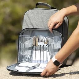 A picnic backpack with grey fabric, containing cutlery, glasses, and plates neatly organised for outdoor dining.
