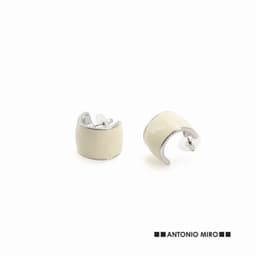 A pair of cream-coloured earrings with a shiny silver setting, featuring a curved design. Includes a logo in the corner.