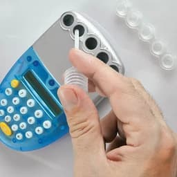 A hand holds a clear funnel above a blue and silver calculator, with a transparent cap visible nearby.