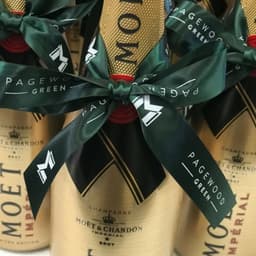 A gold champagne bottle wrapped with a dark green custom printed satin ribbon featuring a logo and text.
