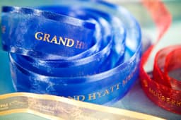 A roll of custom printed organza ribbon in blue, red, and gold, featuring different brands, with satin edges.