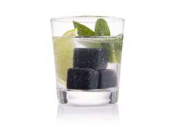 A glass containing a refreshing drink with black gin stones, mint leaves, and lime slices.