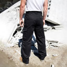 Black action trousers featured against a construction backdrop, showcasing functional pockets and a durable design.