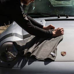 A grey drying towel laid on the bonnet of a car, with a person preparing to use it. The car has a logo.