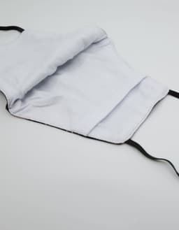 A black face mask made from 100% cotton with an inner lining showing. It features elastic ear straps and a label.