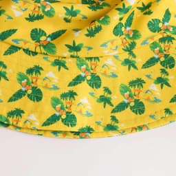 A vibrant yellow bucket hat with a tropical pattern featuring green leaves and floral accents. It has a logo on the side.
