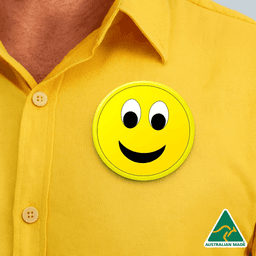 A yellow button badge with a smiling face placed on a yellow shirt. Features an Australian Made logo.