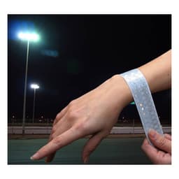 A reflective slap wristband in silver is shown on a person's wrist, illuminated by bright lights in the background.