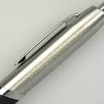 A silver pen with a black grip and a metal clip, featuring branding on the barrel.
