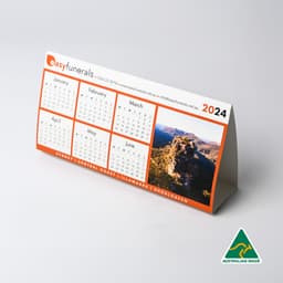 A desk calendar for 2024 with a scenic image, featuring an orange and white design, and a logo.